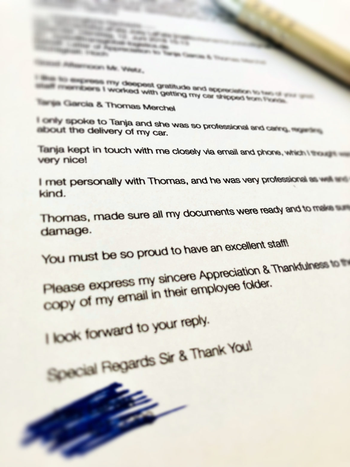 Ein Foto eines gedruckten Briefes mit einem blauen Stift auf der rechten Seite. Der Text beschreibt Dankbarkeit und Anerkennung für die professionelle Unterstützung bei der Lieferung eines Autos. Unten im Bild ist ein Teil des Texts geschwärzt.