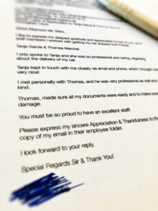 Ein Foto eines gedruckten Briefes mit einem blauen Stift auf der rechten Seite. Der Text beschreibt Dankbarkeit und Anerkennung für die professionelle Unterstützung bei der Lieferung eines Autos. Unten im Bild ist ein Teil des Texts geschwärzt.